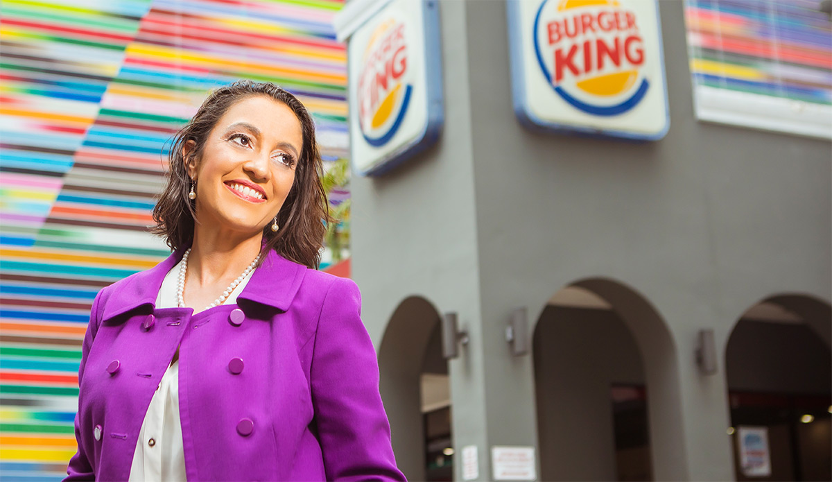 Grissel Seijo in a purple suit jacket and standing in front of a Burger King Sign