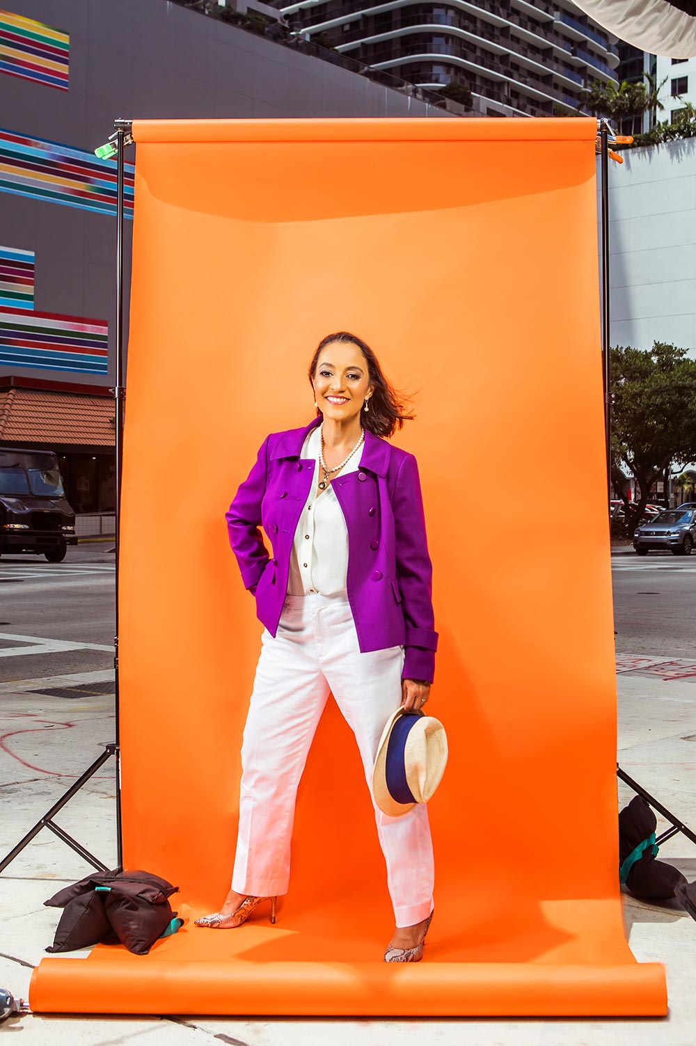 Grissel Seijo in a purple suit jacket and white pants, standing in front of a bright orange photoshoot screen