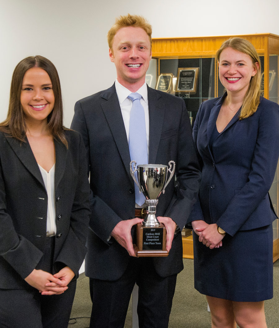 three Fordham law students standing together with a trophy