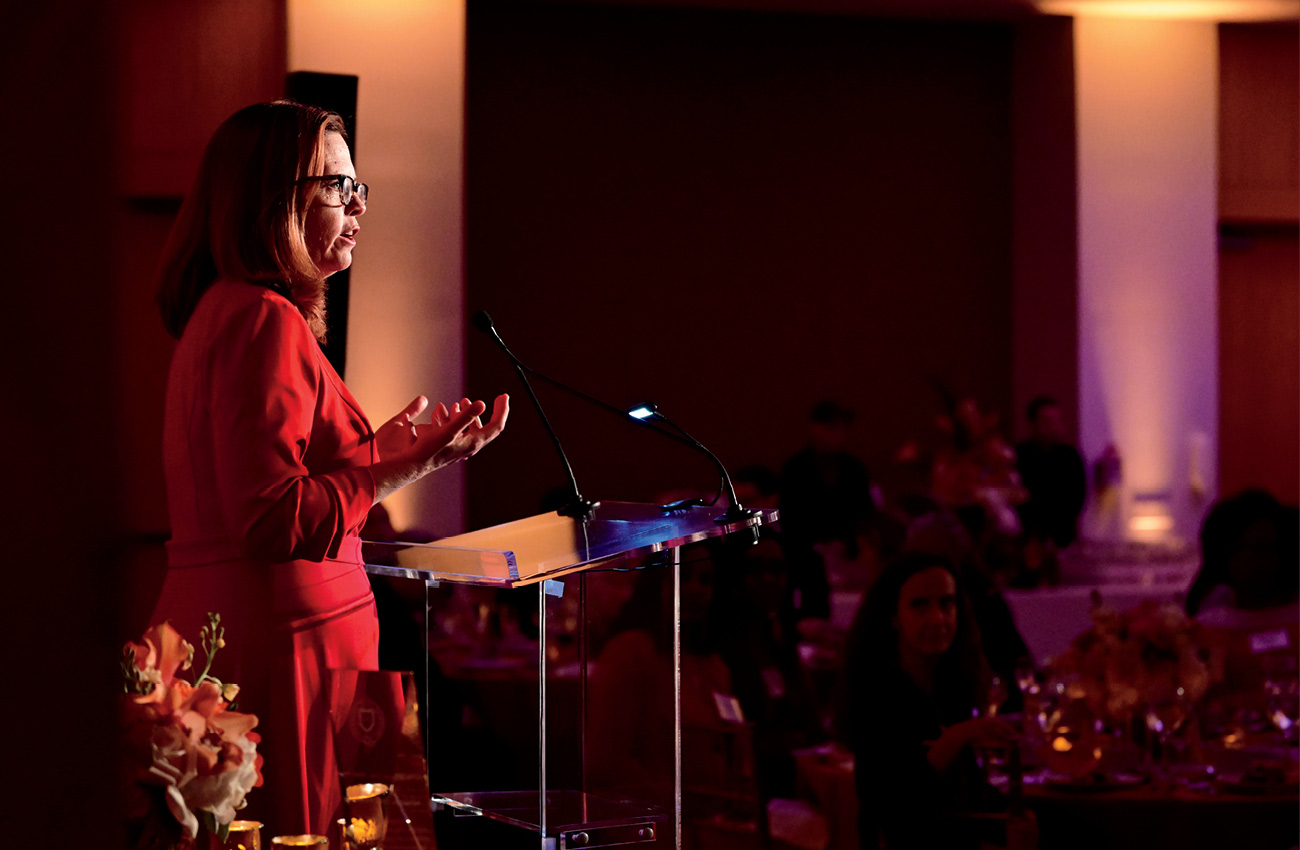 Fordham University President Tania Tetlow in red dress speaking at event