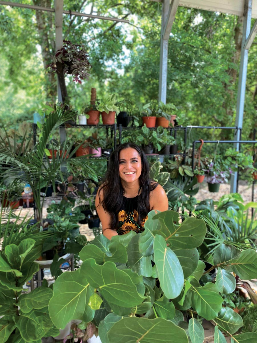 a picture of Erandi Trevino wearing a black shirt with a sunflower design surrounded by various types of green plants