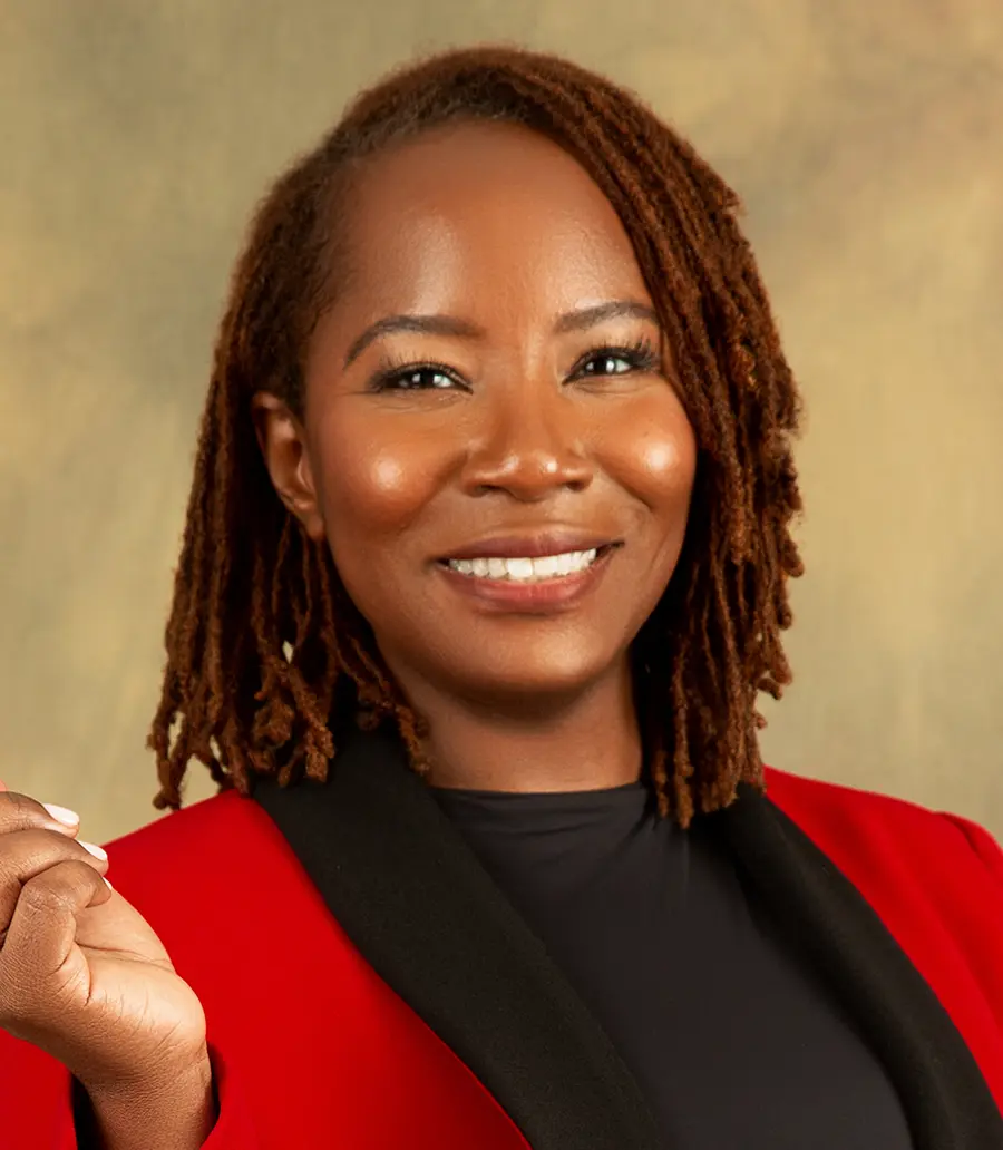 Portrait orientation photograph headshot of Ritha Pierre, a smiling woman in a dark red business blazer suit and black blouse underneath