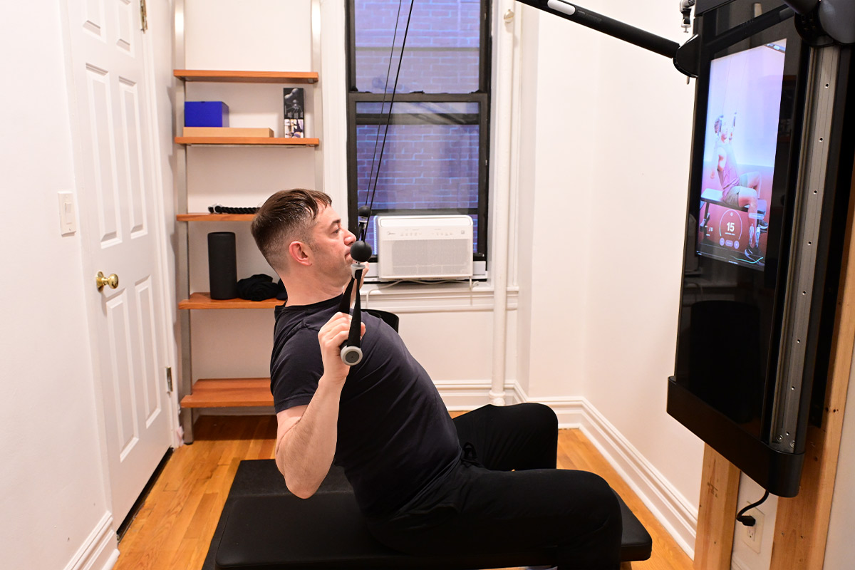Joseph Landau uses a cable pulley machine in a small room with a screen displaying graphics.