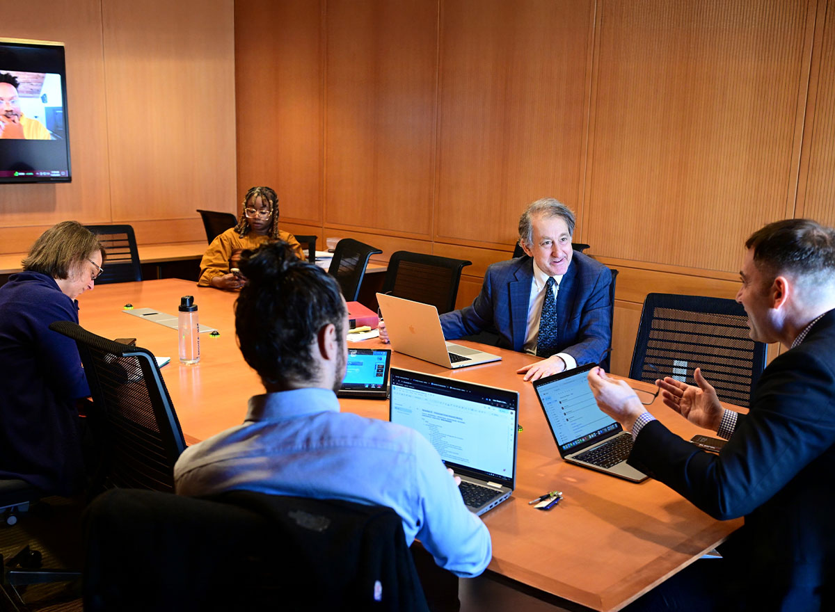 Dean Joseph Landau and three colleagues seated around a conference table with laptops during a meeting