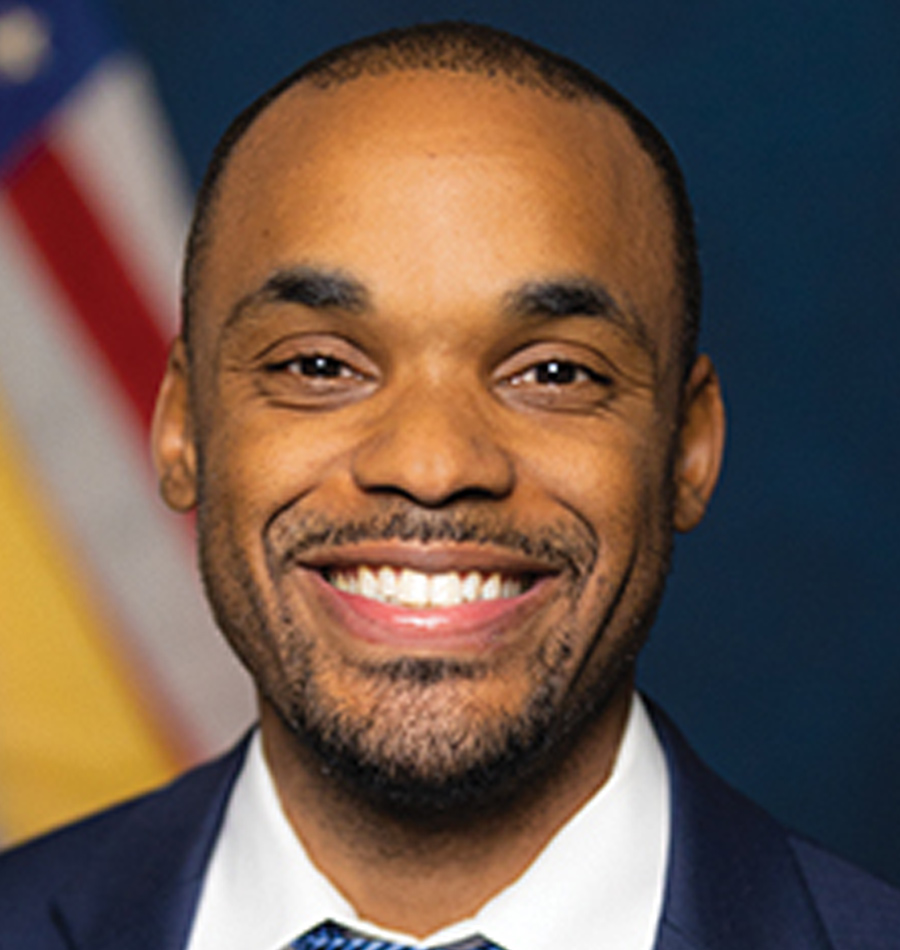 Headshot of Derick Dailey smiling in a navy blue business blazer suit