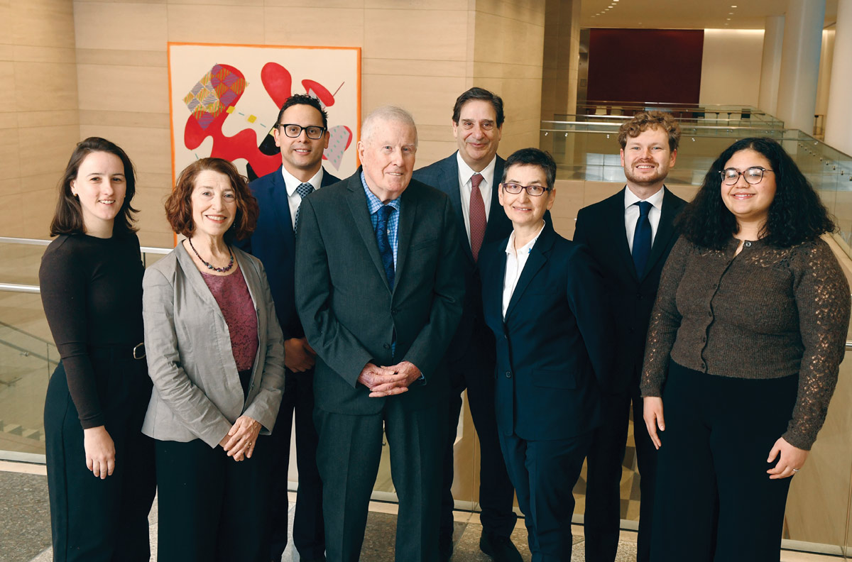 A group of eight people in professional attire posing for a photo in a modern building with abstract art behind them.