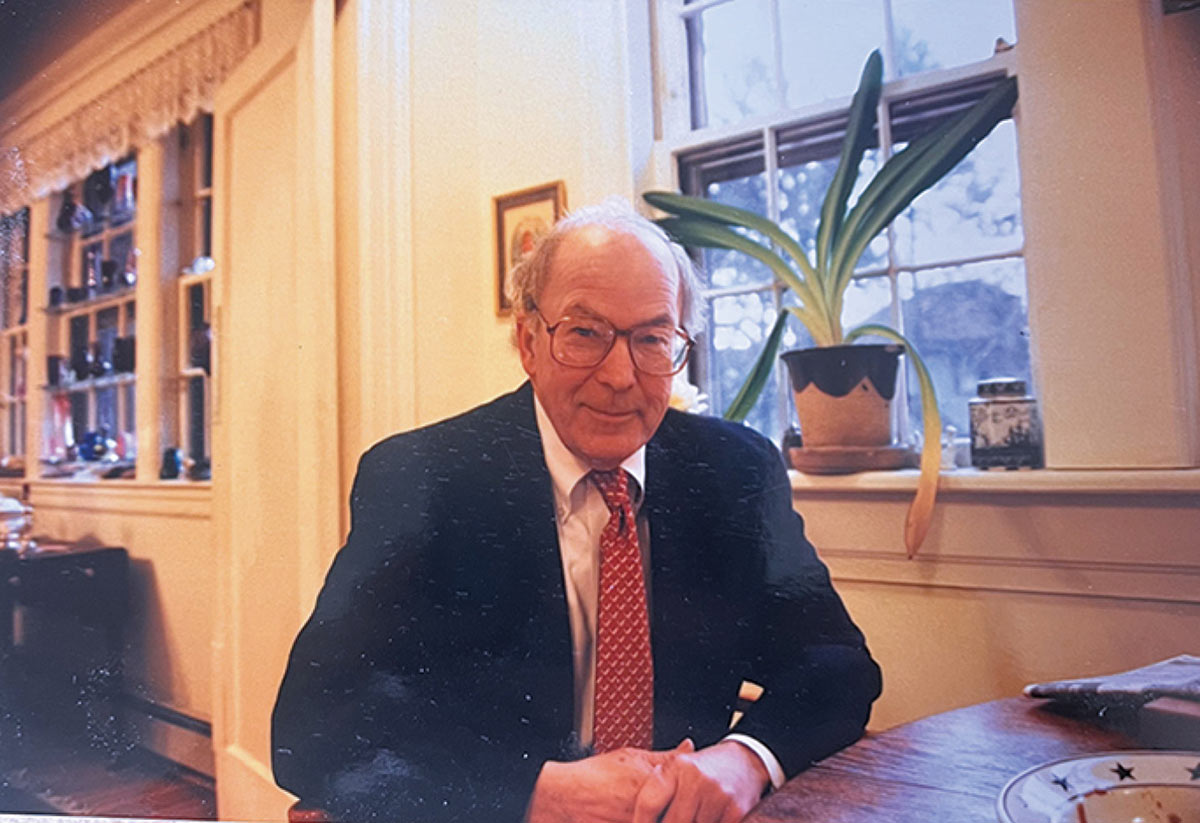 Rev. Dr. Romaine L. Gardner wearing glasses, a dark suit, and a red patterned tie sitting at a wooden table