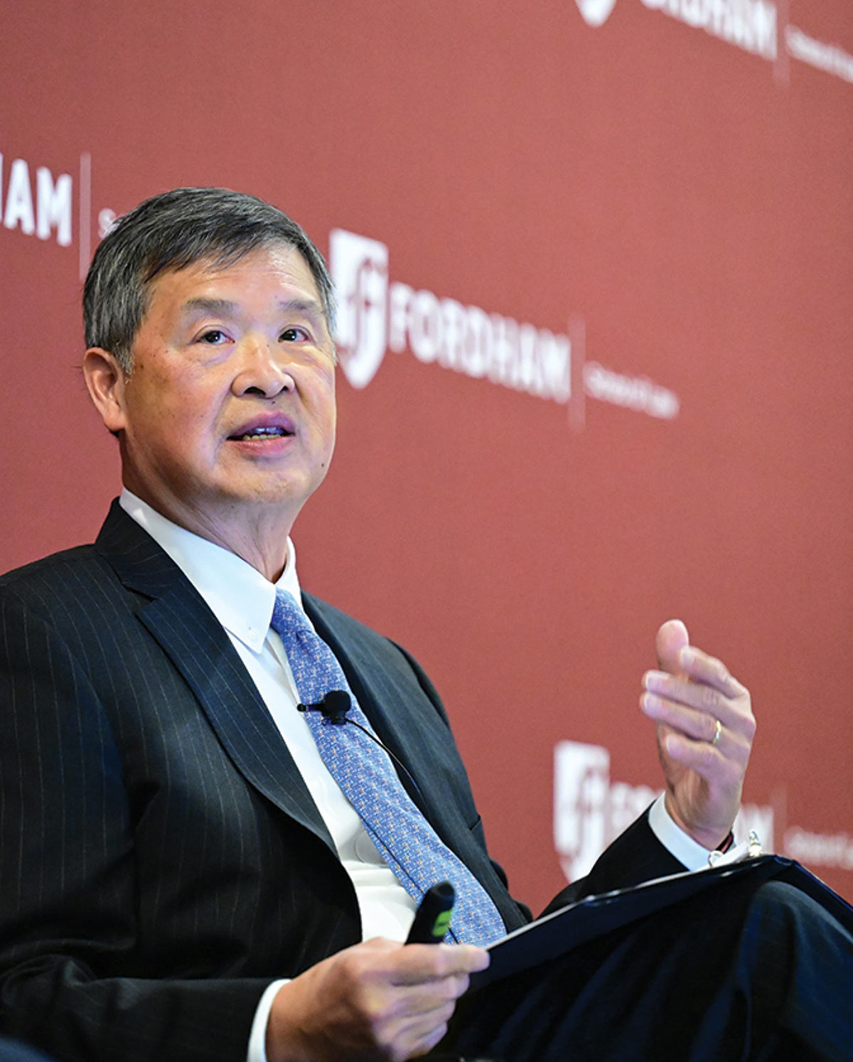 Denny Chin in a pinstripe suit and blue tie gesturing while speaking at a Fordham event