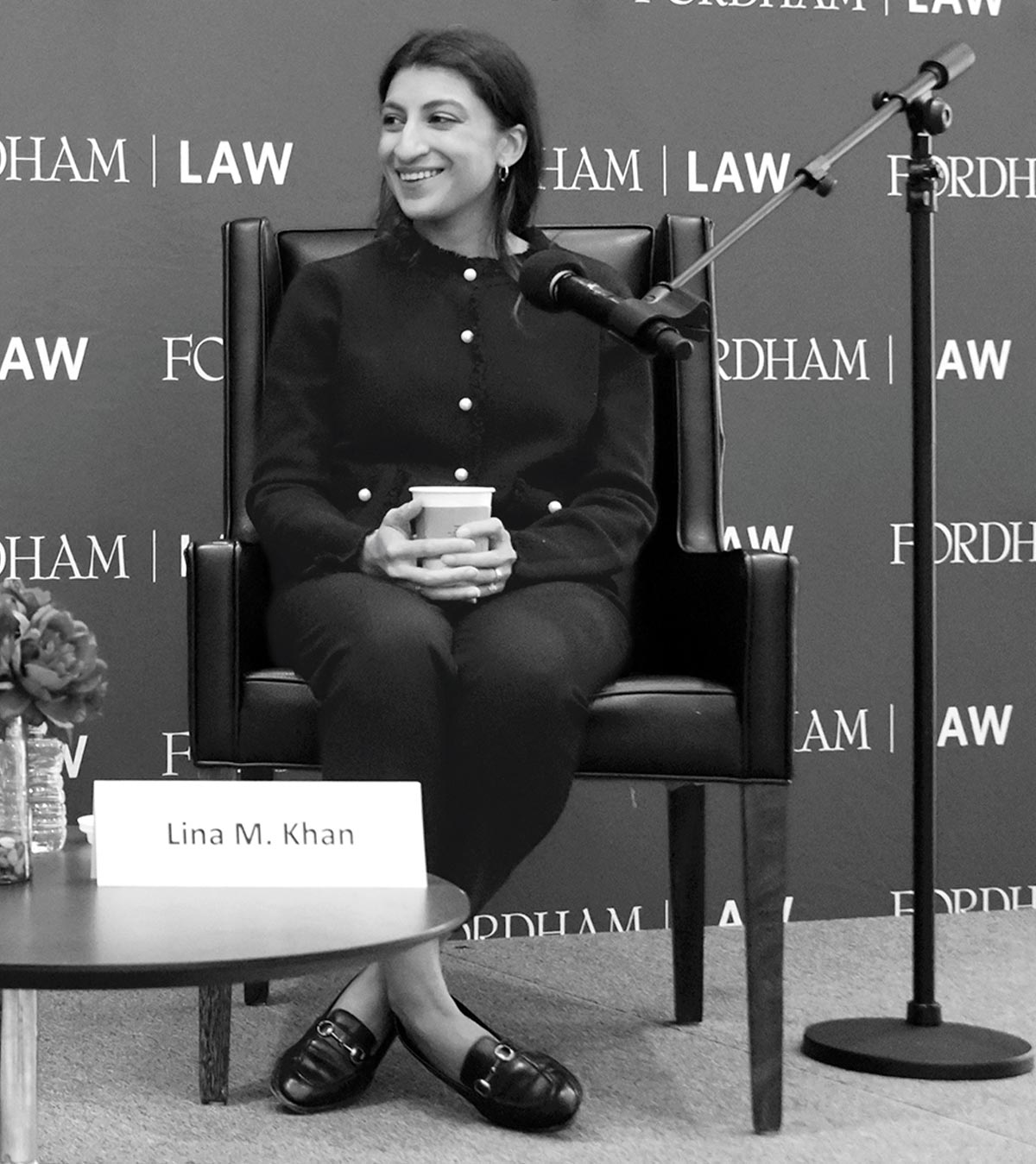 Black and white photo of Lina M. Khan smiling in a leather chair at a Fordham Law event