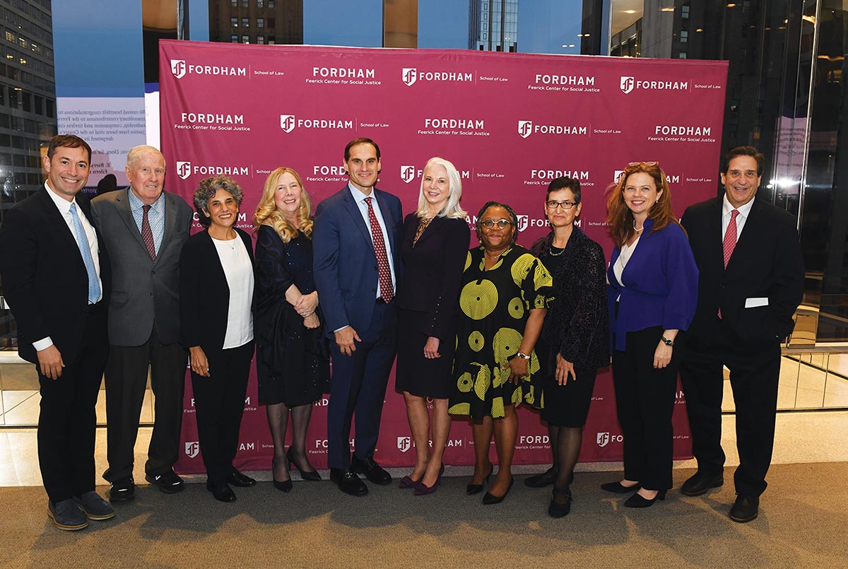 Ten people in professional attire pose for a group photo in front of a maroon Fordham Law backdrop featuring the Feerick Center for Social Justice logo.