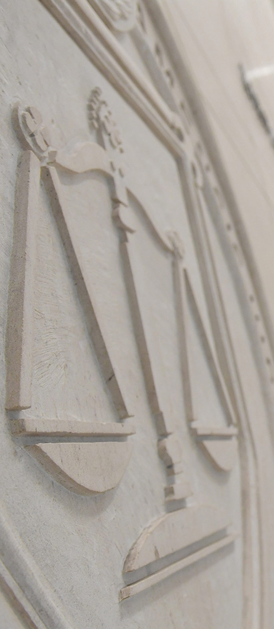 Angled close-up of a stone relief carving showing balanced scales of justice on a wall