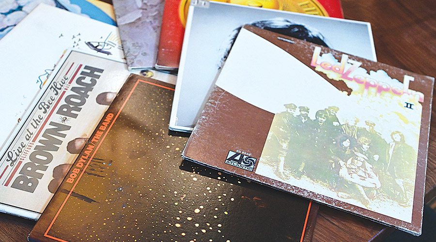 A collection of vinyl record albums scattered on a wooden surface. Visible covers include "Led Zeppelin II," Clifford Brown and Max Roach’s "Live at the Bee Hive," and an album by Bob Dylan and The Band.