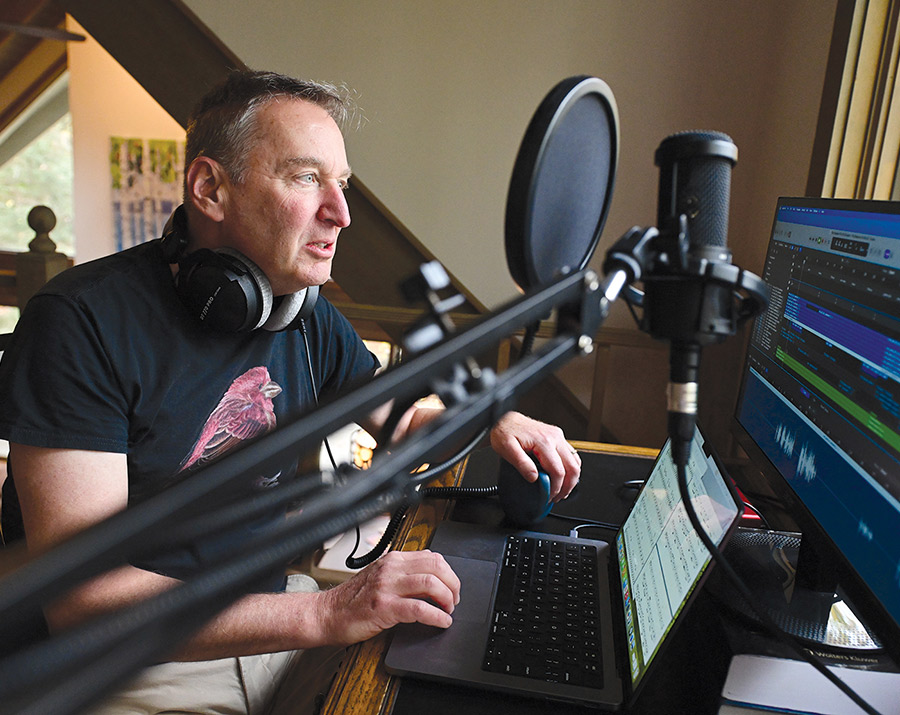 Professor Howard Erichson sits at a desk wearing headphones and speaking into a microphone. He looks at a monitor displaying audio editing software while a laptop in front of him shows musical notation.