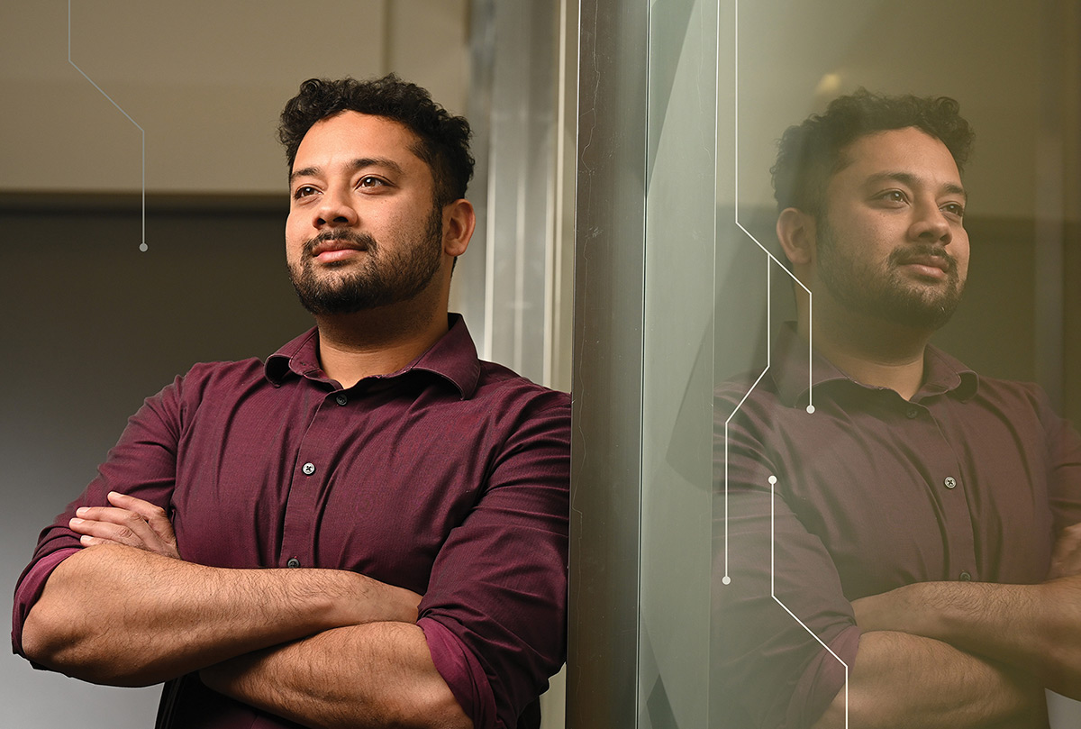 Professor Aniket Kesari stands with arms crossed, leaning against a glass wall that reflects him.
