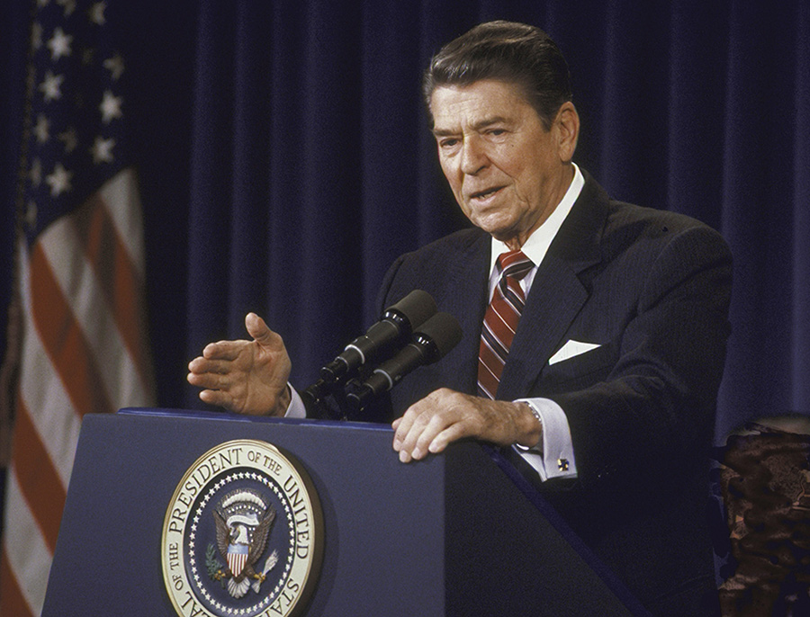 President Ronald Reagan gestures while speaking from a podium featuring the Presidential Seal.