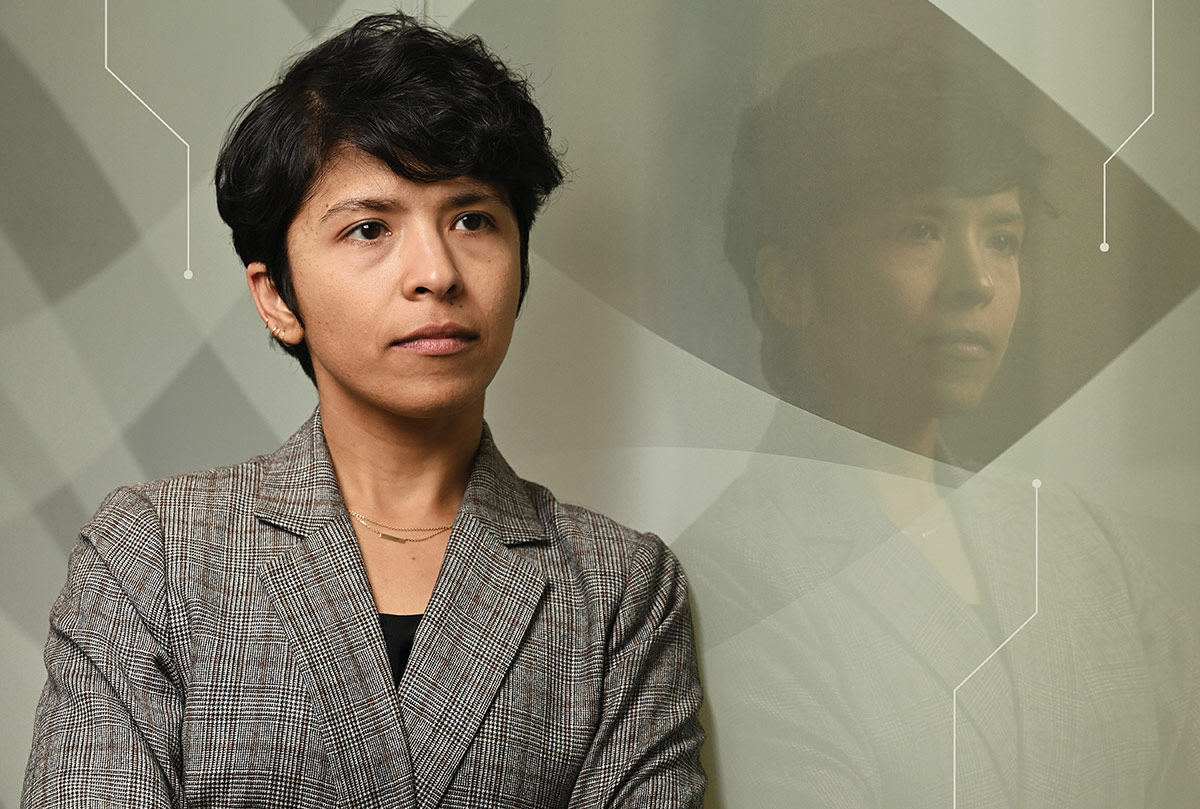 Professor Chinmayi Sharma poses in a blazer, leaning against a glass wall with her reflection.