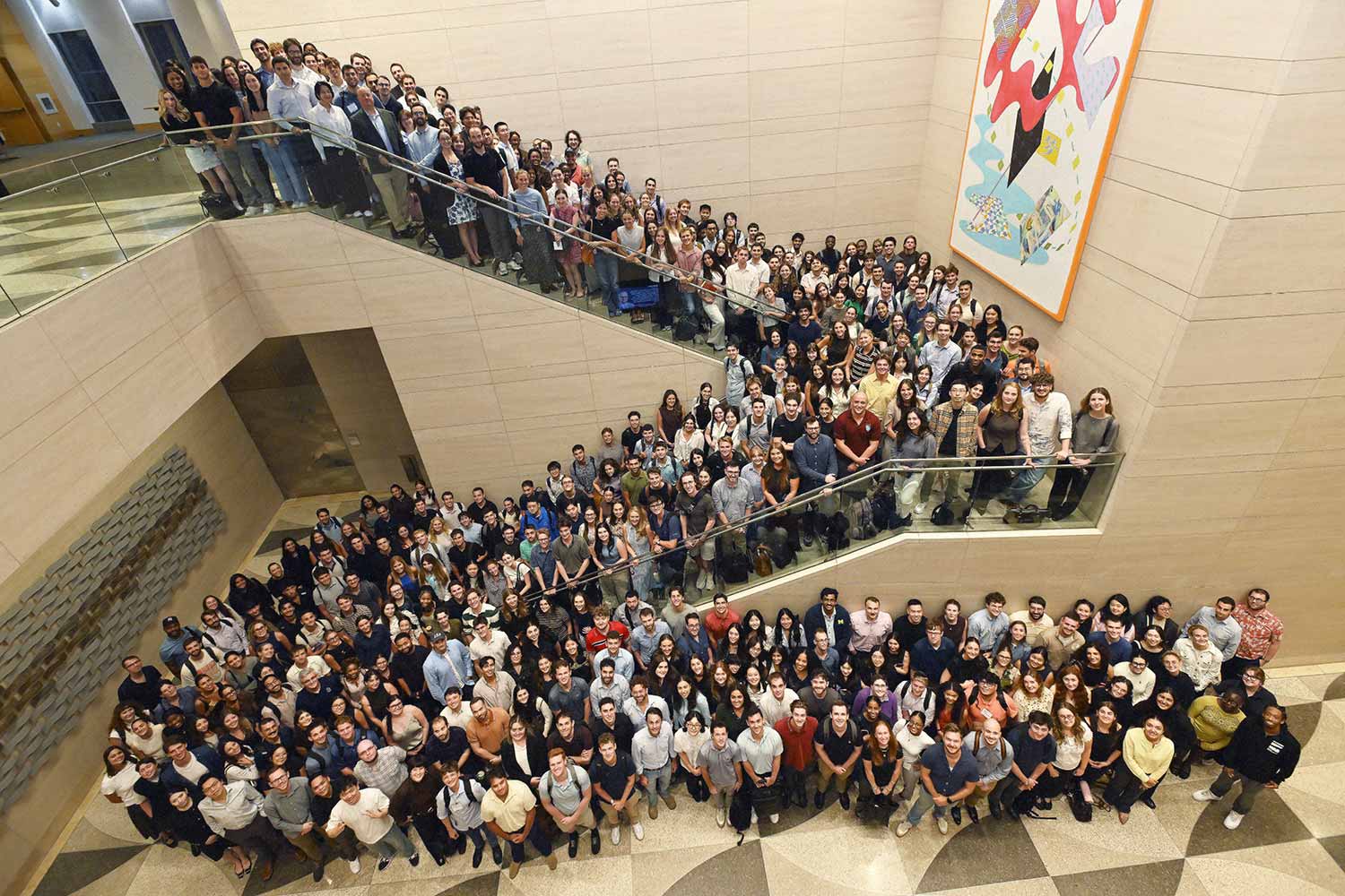 Large group photo of students gathered on a wide staircase and modern atrium floor.